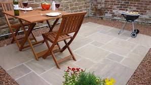 Une table et des chaises en bois sont disposées sur une terrasse, avec un mur de pierres et un mur de briques en arrière-plan.