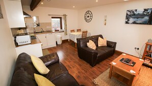 A living room with a brown leather sofa, a wooden coffee table, and a dining area with a table and chairs. - Milecastle, Irthington , ideal for couples or families exploring Hadrians Wall (Irthington)