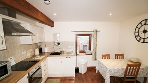 A compact kitchen with white cabinets, a wooden countertop, a built-in oven, and a dining area with a table and chairs. - Milecastle, Irthington , ideal for couples or families exploring Hadrians Wall (Irthington)