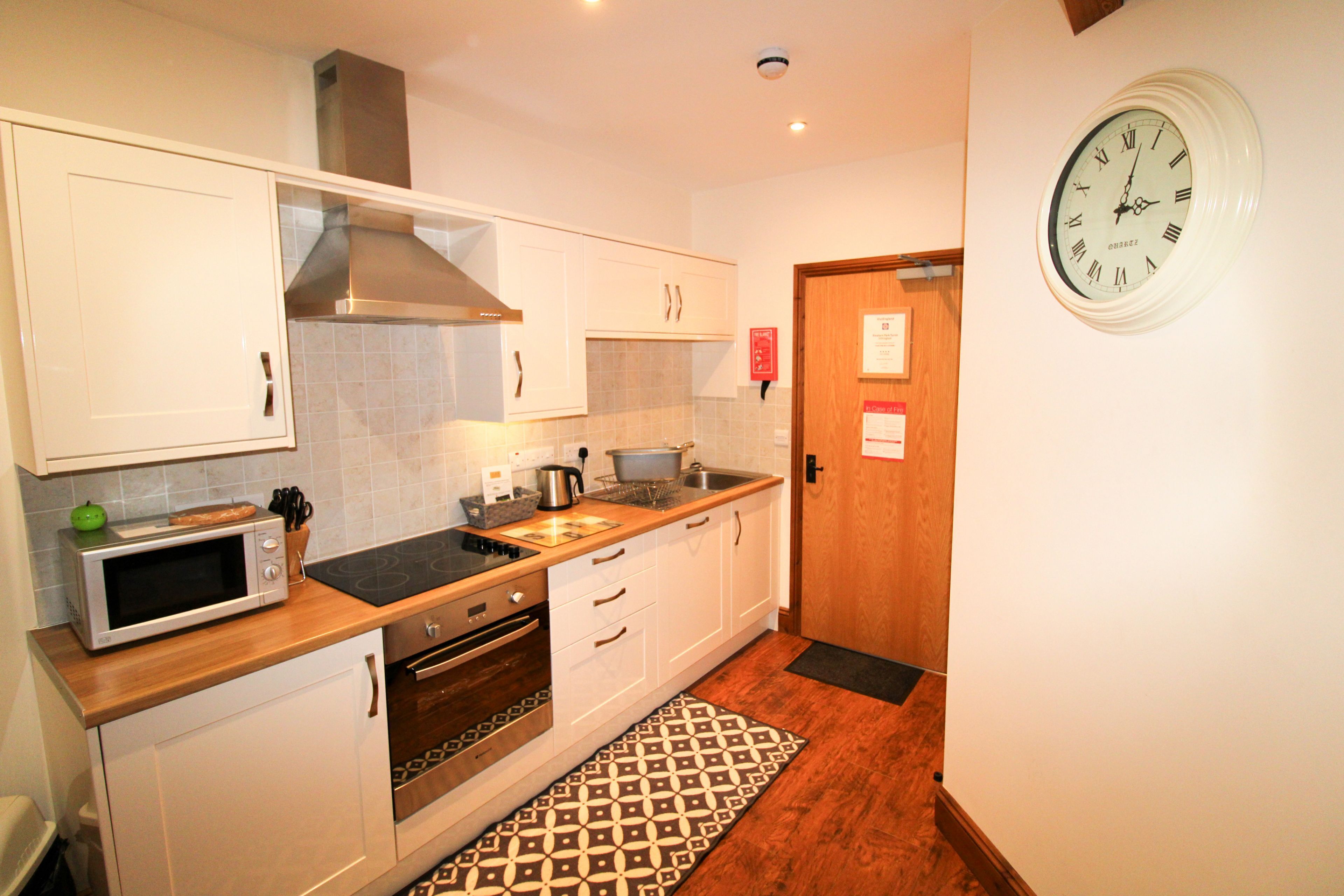A modern kitchen with white cabinets, a microwave, an oven, and a clock on the wall.