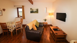 Ein Wohnzimmer mit einem Holzesstisch, einem schwarzen Ledersofa, einem an der Wand montierten Fernseher und einer Lampe.