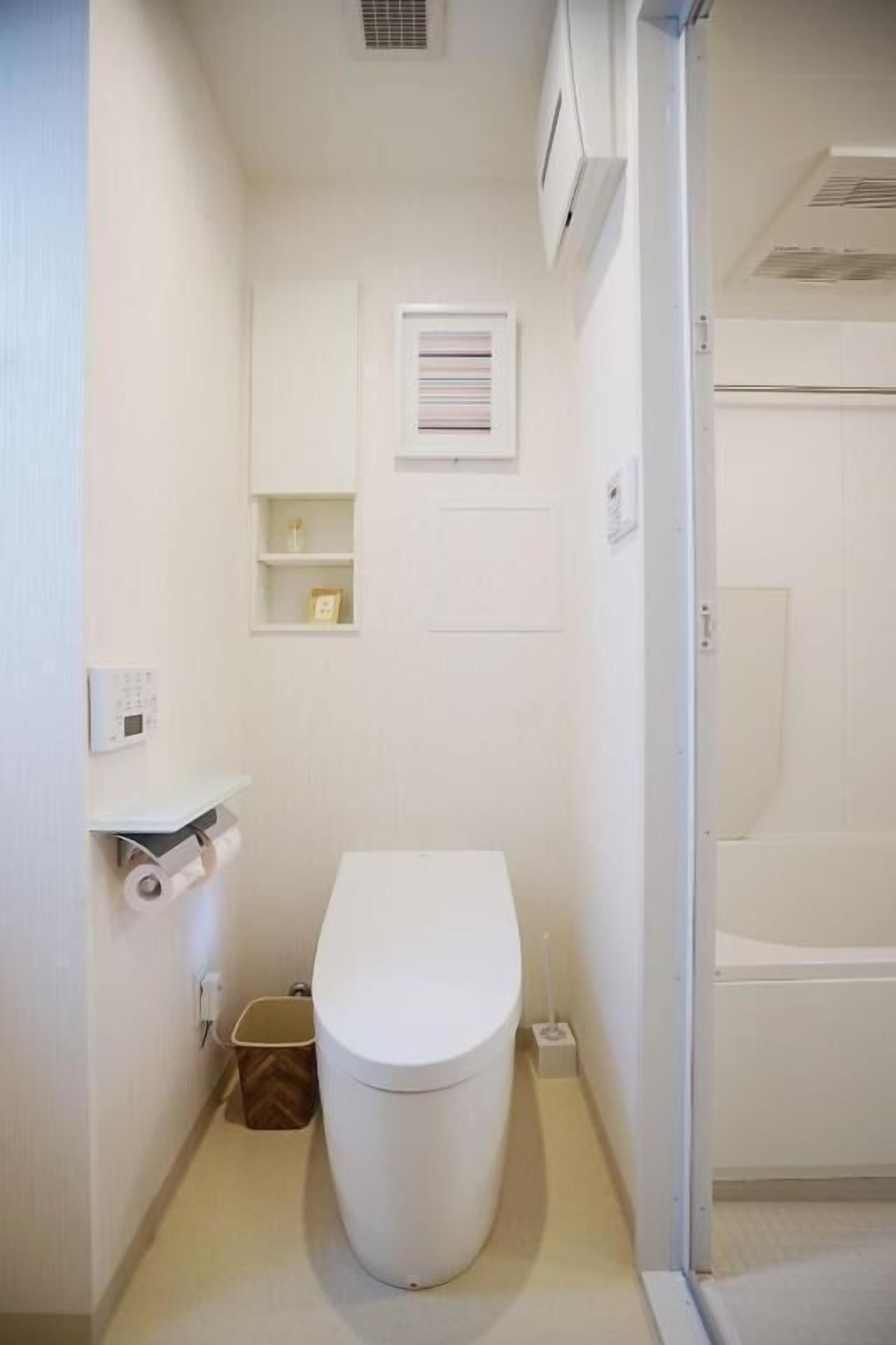 Un baño pequeño y blanco con inodoro, un estante con artículos de aseo y una zona de ducha.