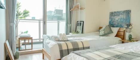 A hotel room with two beds, a balcony, a painting, and a small table with a plant.
