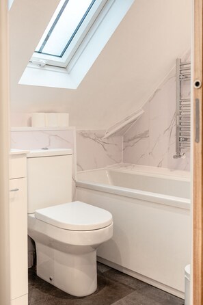 A modern bathroom with a skylight, a toilet, a bathtub, and marble walls. - Beautiful 2 Bedroom Apartment in Malvern (Malvern)