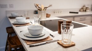 A modern kitchen with white countertops, a central island, and a dining area set with white plates, bowls, and cutlery. - Beautiful 2 Bedroom Apartment in Malvern (Malvern)