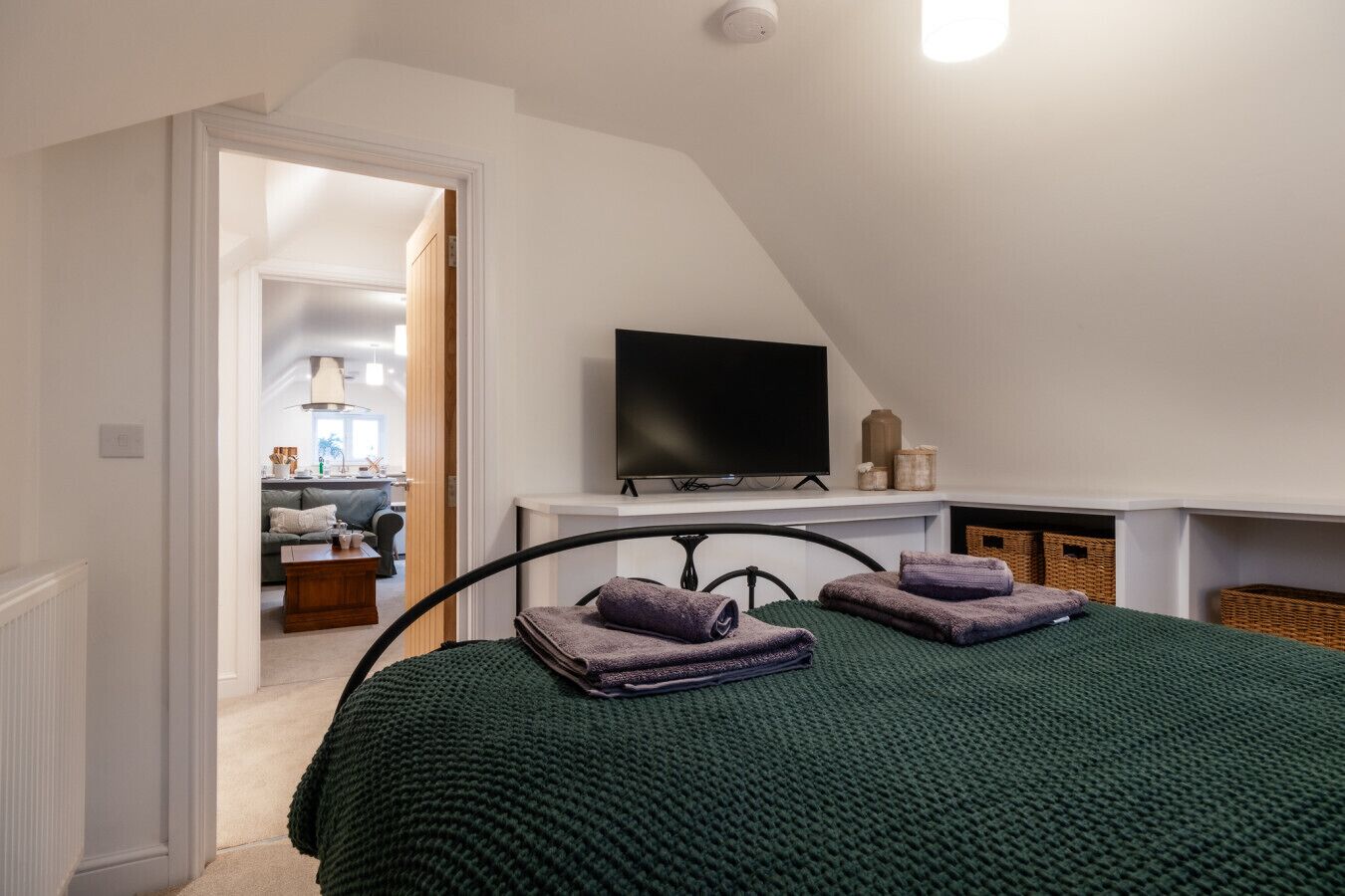 A bedroom with a bed, a television, and a view into the living area.