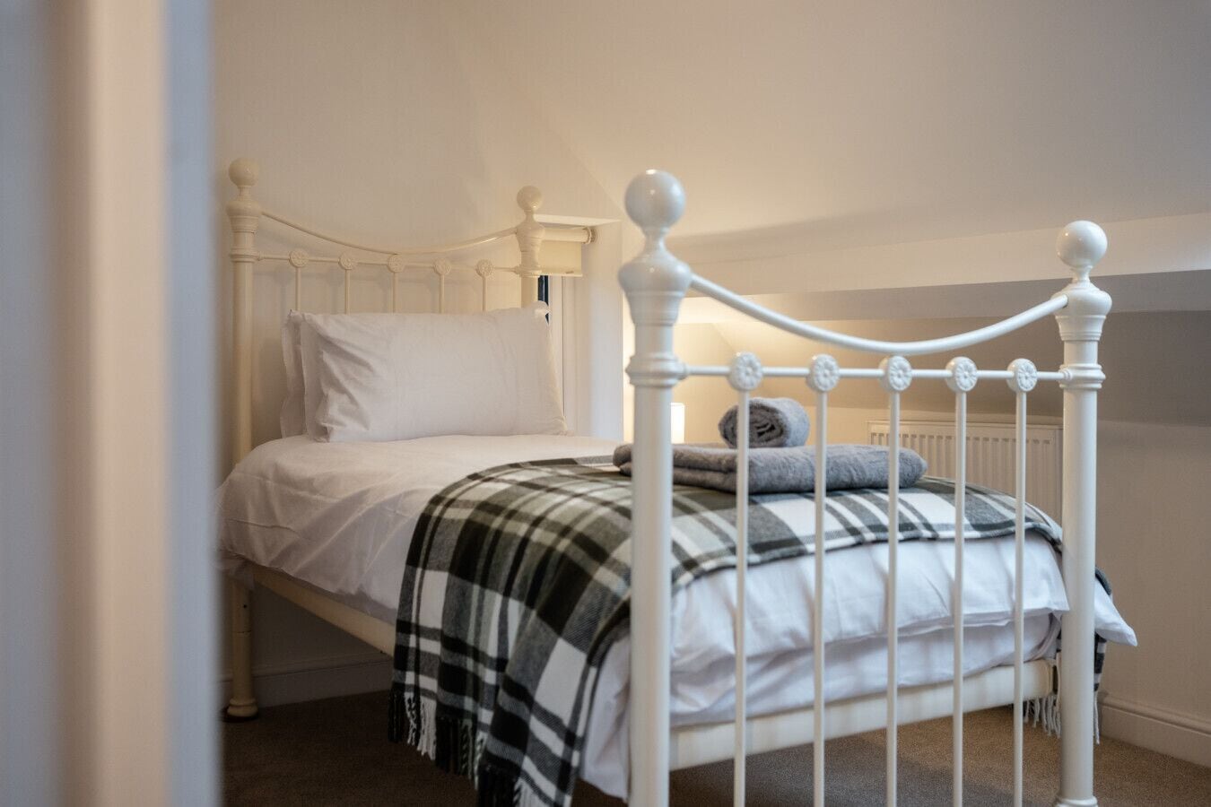 Un lit simple avec un cadre en métal blanc et une couverture à carreaux.