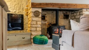 A cozy living room with a stone wall, a wooden beam ceiling, a television, a sofa, a green bean bag, and a wood-burning stove. - Fleur de Lys - Beautiful Home in the Heart of Winchcombe (Winchcombe)