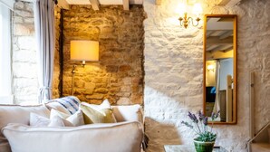 A cozy room with a stone wall, a white sofa, a lamp, and a mirror. - Fleur de Lys - Beautiful Home in the Heart of Winchcombe (Winchcombe)