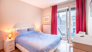 Ein Schlafzimmer mit Bett, Nachttischen, einem Schminktisch und einem Balkon mit roten Vorhängen.