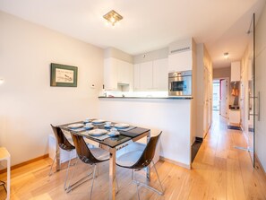 Eine moderne Küche mit weißen Schränken, einem Edelstahlbackofen und einem Essbereich mit einem Glastisch und Metallstühlen.