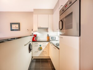A modern kitchen with white cabinets, a stainless steel oven, a microwave, and a coffee maker. - Nice apartment with balcony in the village (Koksijde)