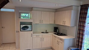 A compact kitchen with a microwave, sink, and stove, light-colored cabinets, and a window with curtains. - Bright 5P Bungalow in Limburg (Simpelveld)