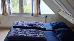 A small, single-room apartment with a loft-style ceiling, a bed with blue bedding, and a window with curtains. - Bright 5P Bungalow in Limburg (Simpelveld)