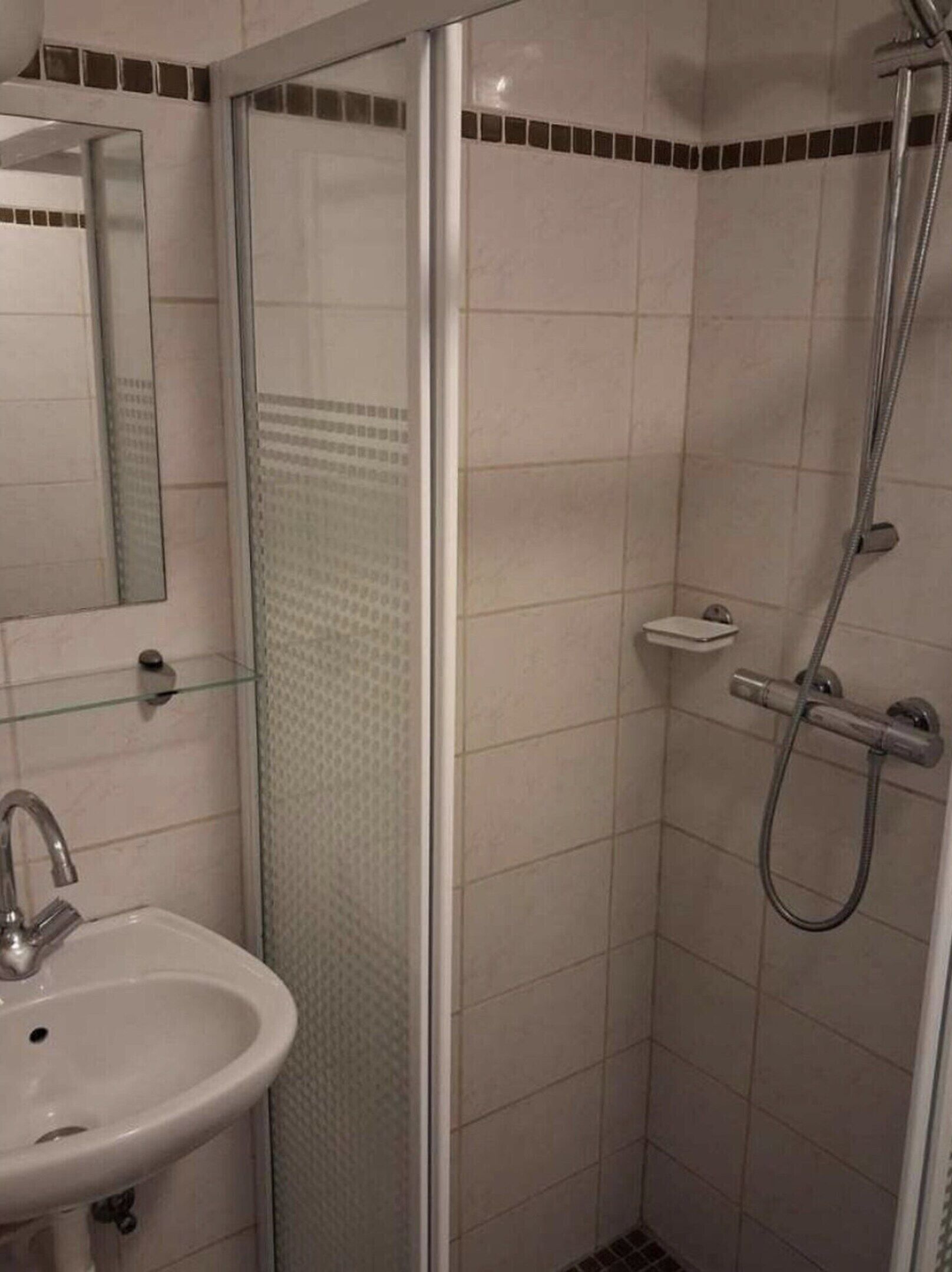 Ein Badezimmer mit Duschkabine, Waschbecken und Spiegel.