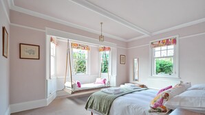 Un dormitorio con una cama grande, una silla colgante y un ventanal con vistas a la vegetación.