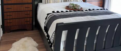 A bedroom with a bed, wooden nightstands, a fluffy rug, and wall decor including a wall-mounted animal skull and patterned wall hangings.