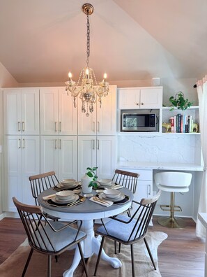 A dining area with a round table set for six, surrounded by chairs, a chandelier, and white cabinets. - NEW - modern comfort, remodeled, A/C, free parking (Seattle)