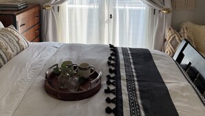 Un letto rifatto con cura, un vassoio con bicchieri, una piccola pianta, una lampada da comodino e un arazzo appeso al muro.