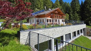 A chalet with a stone facade, a wooden upper level, and a balcony with flowers.