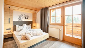 A wooden cabin bedroom with a bed, a radiator, a window with curtains, and a wall-mounted light fixture.