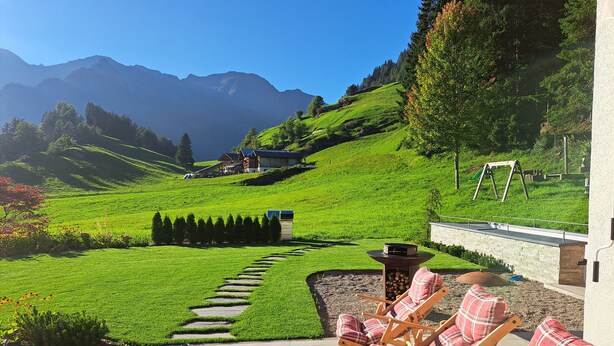 A patio with outdoor seating, a fire pit, and a view of a green hillside with a house in the background.