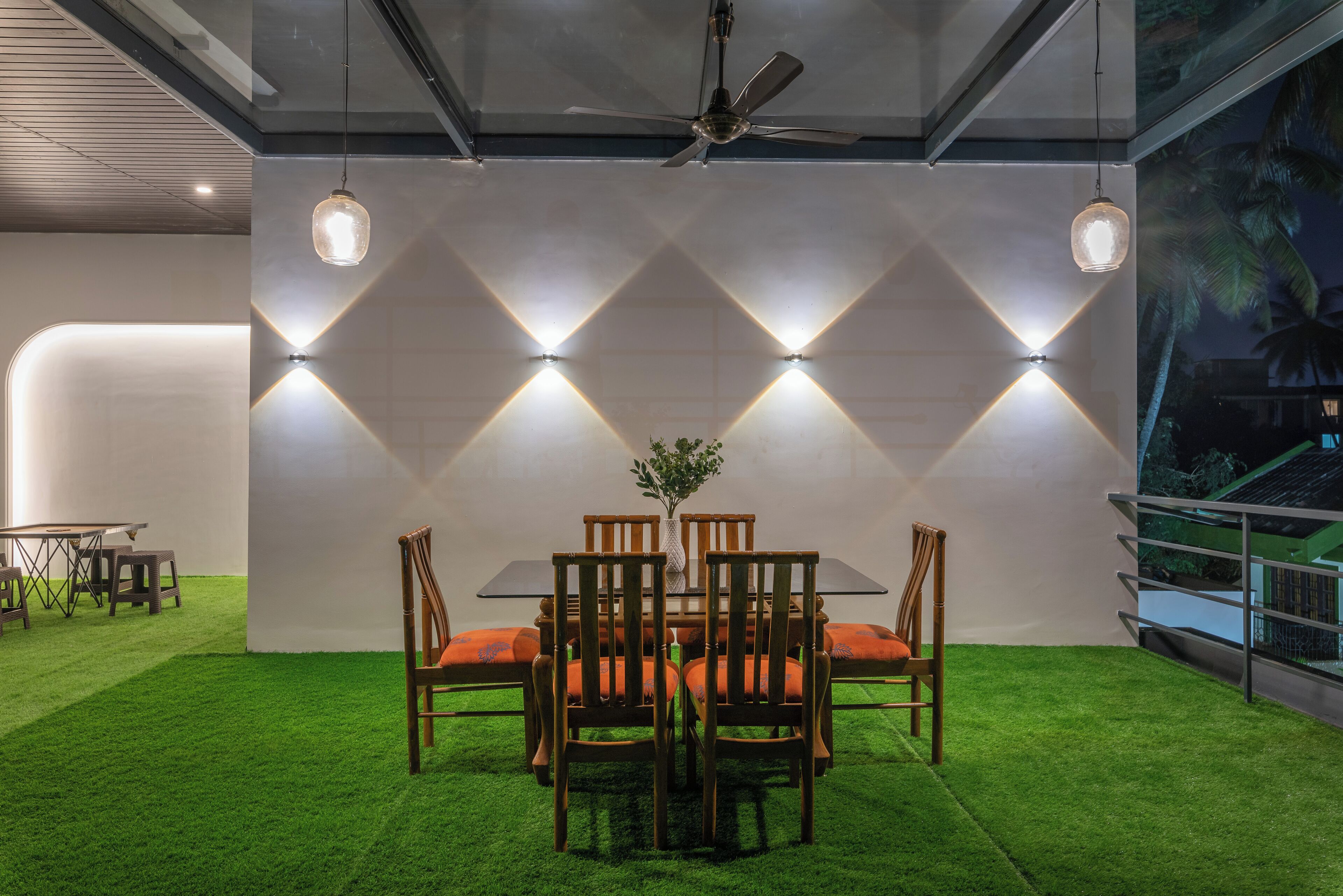 Een eethoek met een tafel, stoelen, een plafondventilator en een decoratieve wand met verlichte panelen.