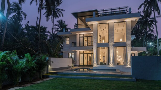 Una casa moderna de dos pisos con un balcón grande, una piscina y exuberante vegetación tropical.