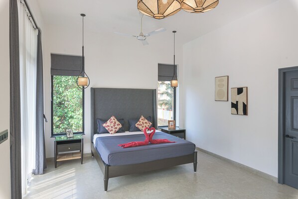 A modern bedroom with a large bed, two bedside tables, a ceiling fan, and artwork on the walls. - Villa Calangute Phase 6 (Calangute)