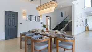 Un comedor con una mesa rectangular y seis sillas, una araña y una escalera al fondo.