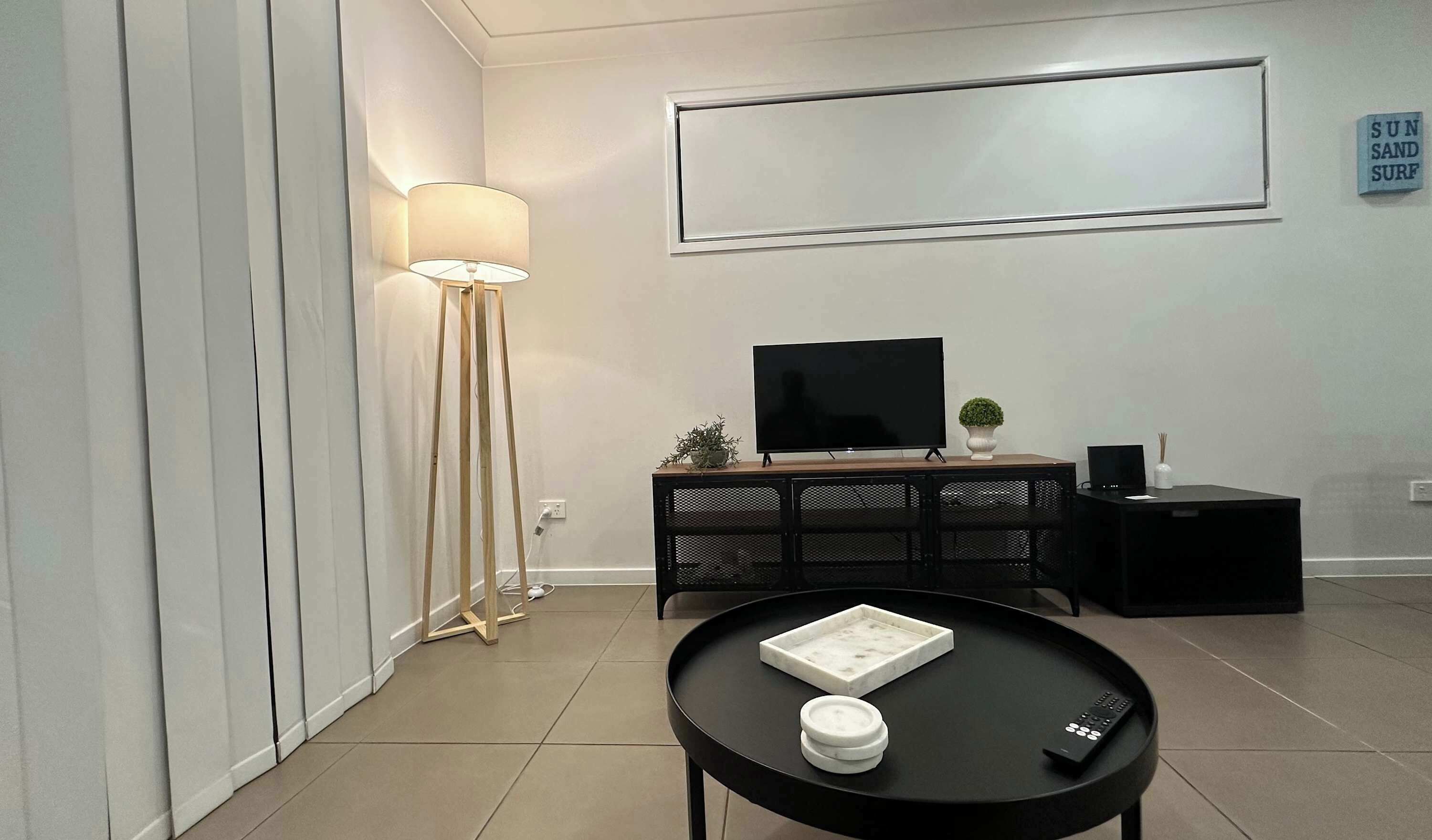 A modern living room with a flat-screen TV, a round coffee table, a floor lamp, and a minimalist console table.