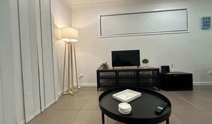 A modern living room with a flat-screen TV, a round coffee table, a floor lamp, and a minimalist console table.
