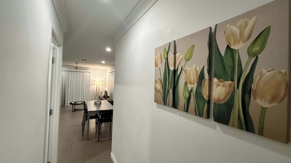 A hallway with a dining area, featuring a table and chairs, and three paintings of tulips on the wall.