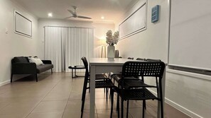 A dining area with a table, chairs, a sofa, a ceiling fan, and a sign reading 'SUN SAND SURF'.