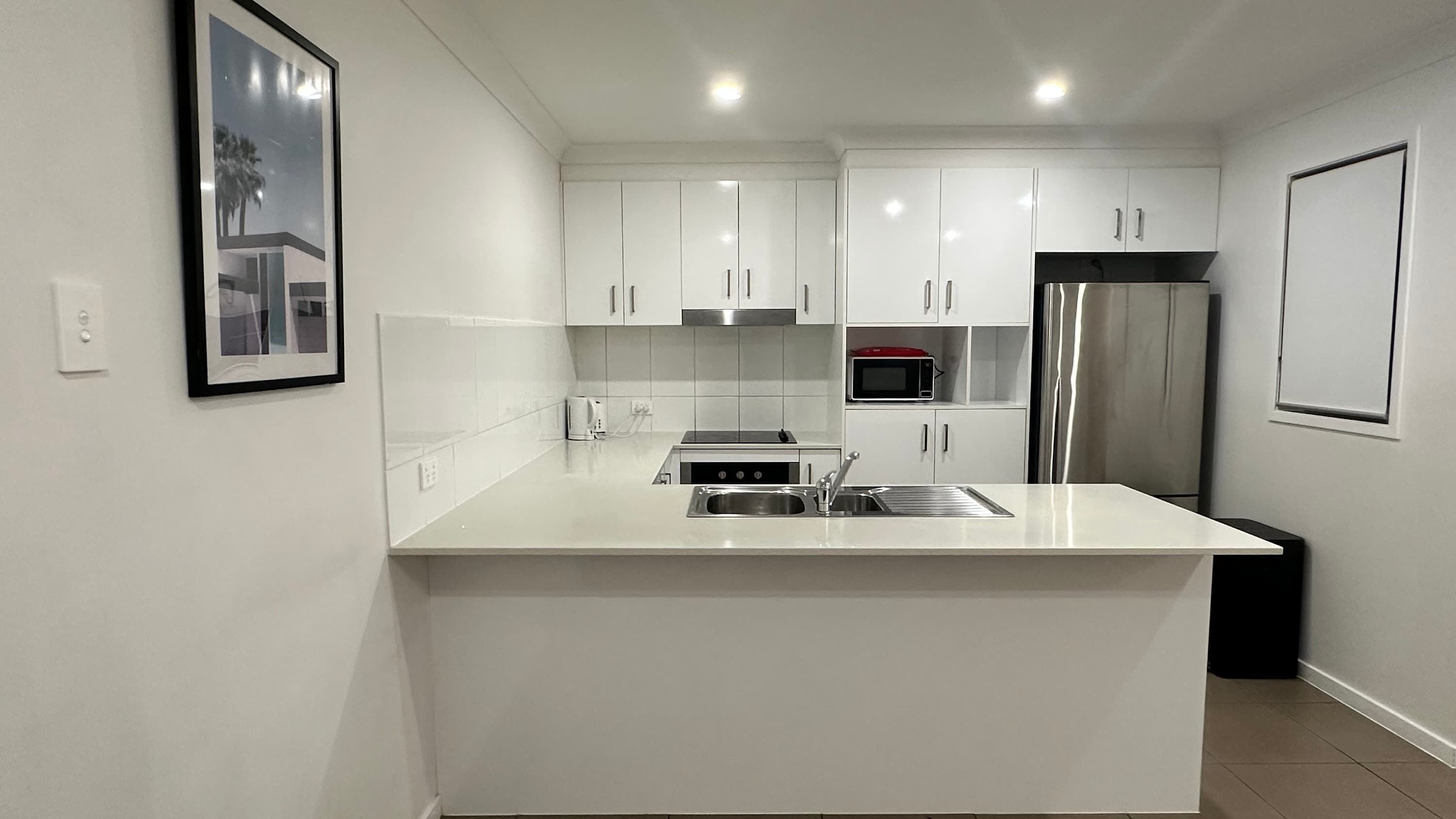 Una cocina moderna con armarios blancos, un lavamanos de acero inoxidable, un microondas y un refrigerador.