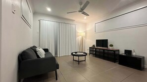 A modern living room with a sofa, a coffee table, a TV on a stand, and a ceiling fan.