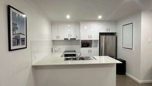 A modern kitchen with white cabinetry, a stainless steel refrigerator, a microwave, and a sink.