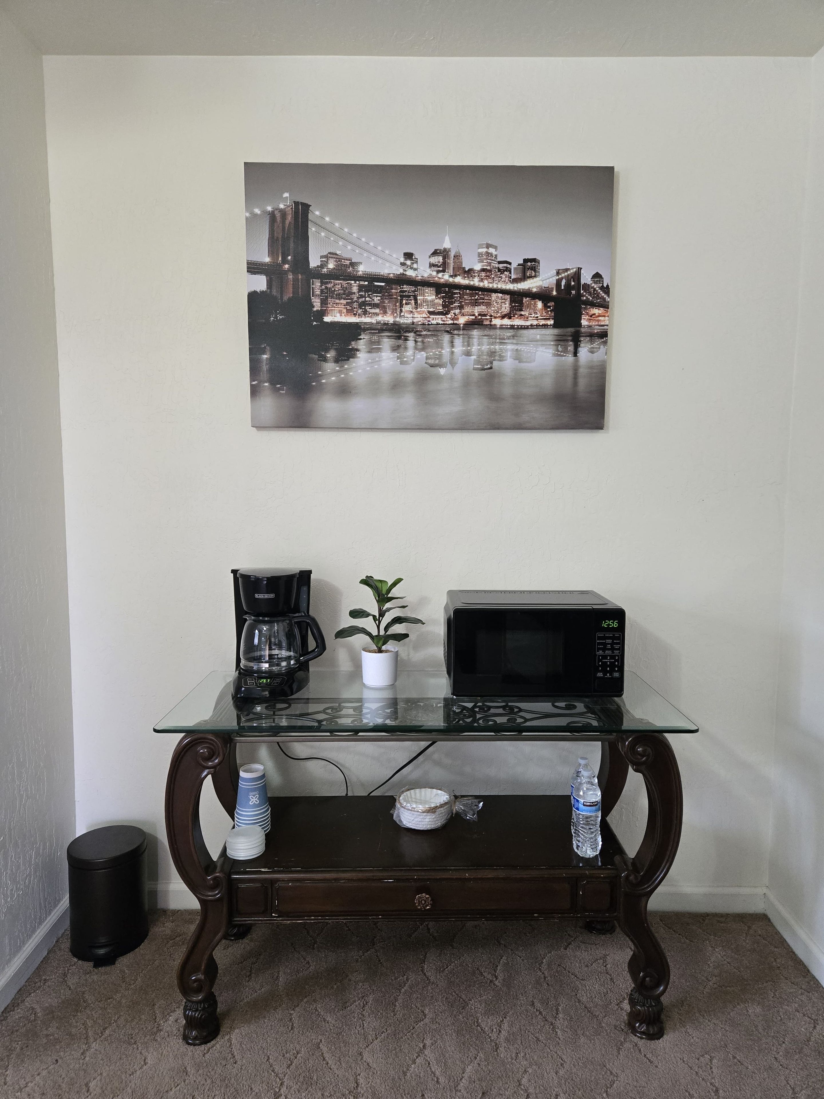 A glass-top coffee table with a microwave and a coffee maker, a potted plant, and a water bottle.