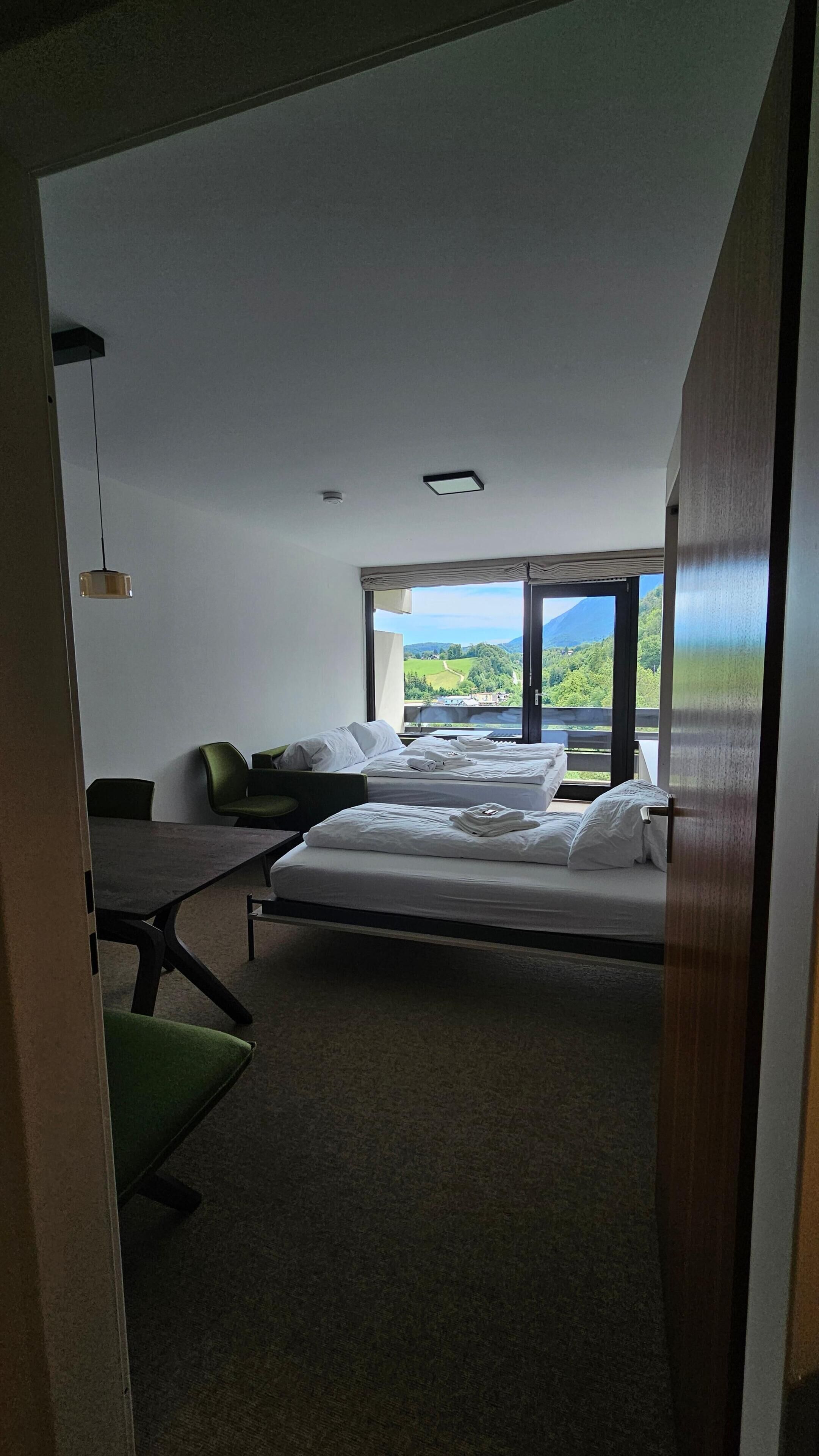 A hotel room with two beds, a desk, and a view of a green landscape.