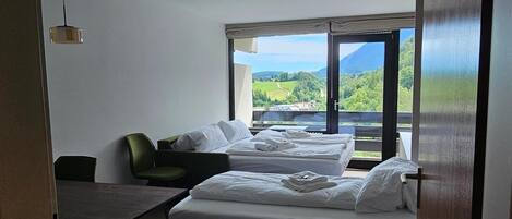 A hotel room with two beds, a desk, and a view of a green landscape.