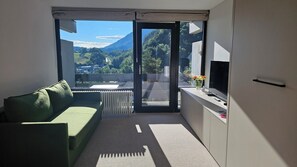 A modern room with a green sofa, a flat-screen TV, and a view of a mountainous landscape through a large sliding glass door. - Vacation apartment Refugium.311 with indoor pool (Bad Reichenhall)