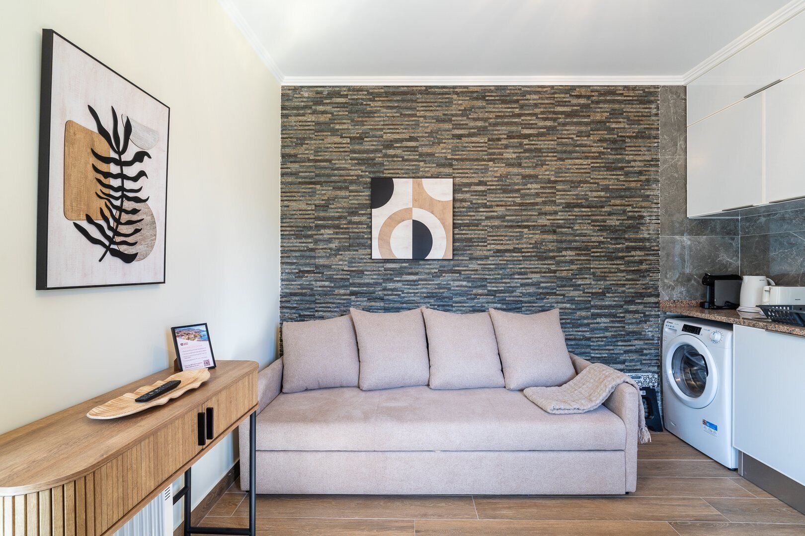 Un salon moderne avec un mur en pierre, un canapé, une petite table en bois et un lave-linge à l’arrière-plan.