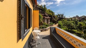 Un bâtiment jaune doté d’un balcon, d’un mur en pierre et d’une petite table entourée de chaises.