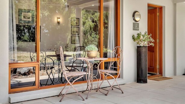A modern outdoor seating area with a glass wall, metal chairs, and a potted plant.