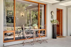 Een modern buitenzitgedeelte met glazen wand, metalen stoelen en een potplant.