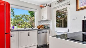 A modern kitchen with white cabinets, a red refrigerator, and a window with a view of trees.