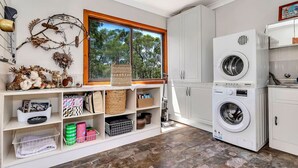 A laundry room with two stacked washing machines, shelves with storage baskets, and a window with a view of trees.