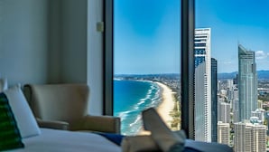Une chambre d’hôtel dotée d’une grande fenêtre donnant sur une plage et des immeubles de grande hauteur.