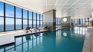 Une piscine intérieure moderne dotée de grandes fenêtres offrant une vue sur l’océan, d’un mur revêtu de marbre et d’un design épuré et minimaliste.