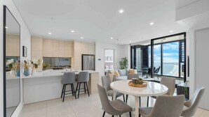 Une cuisine moderne dotée d'un îlot central, d'un coin repas avec des chaises et d'une grande fenêtre offrant une vue sur l'océan.